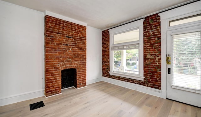 unfurnished living room with a brick fireplace, light hardwood / wood-style floors, brick wall, and ornamental molding