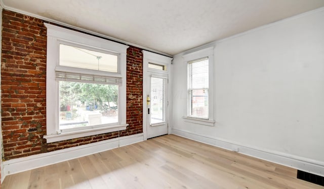 foyer entrance featuring light wood-type flooring, a healthy amount of sunlight, and brick wall