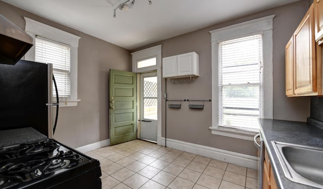 kitchen with stainless steel refrigerator, sink, black gas range oven, track lighting, and light tile patterned floors