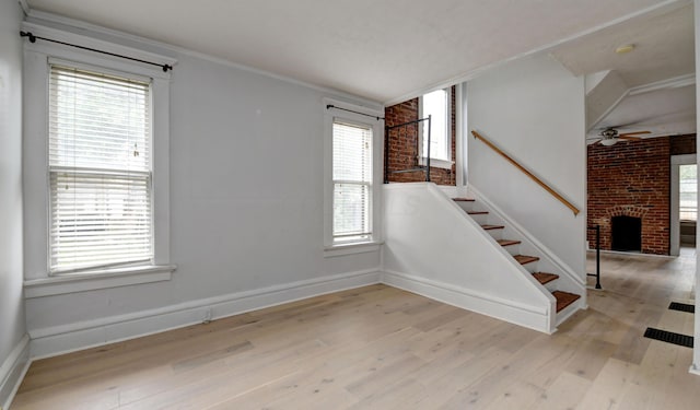 stairs with hardwood / wood-style floors, a brick fireplace, ceiling fan, and plenty of natural light