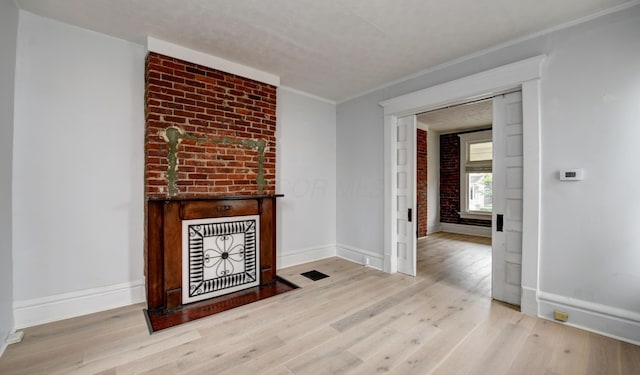 unfurnished living room with light wood-type flooring, ornamental molding, and brick wall