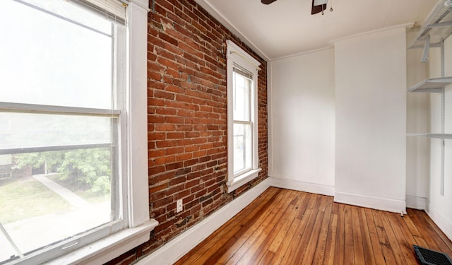 spare room featuring light hardwood / wood-style flooring, ceiling fan, ornamental molding, and brick wall