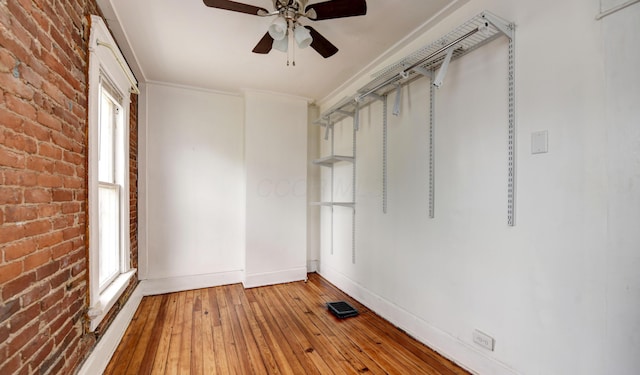 unfurnished room with ceiling fan, light hardwood / wood-style floors, ornamental molding, and brick wall