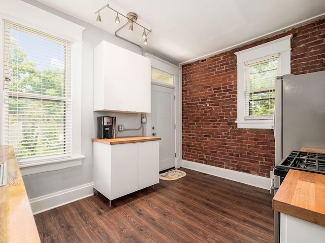 kitchen featuring plenty of natural light, white cabinetry, brick wall, and wooden counters