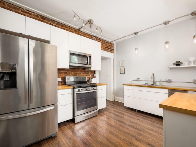 kitchen featuring butcher block countertops, brick wall, decorative light fixtures, and appliances with stainless steel finishes