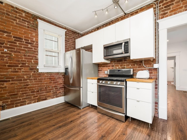 kitchen with wooden counters, white cabinets, appliances with stainless steel finishes, dark hardwood / wood-style flooring, and brick wall