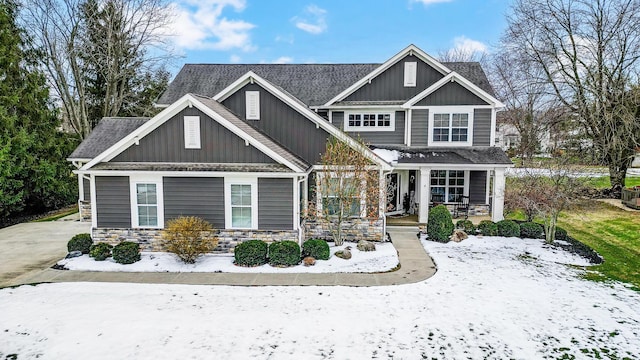 craftsman-style home with stone siding, a porch, board and batten siding, and roof with shingles