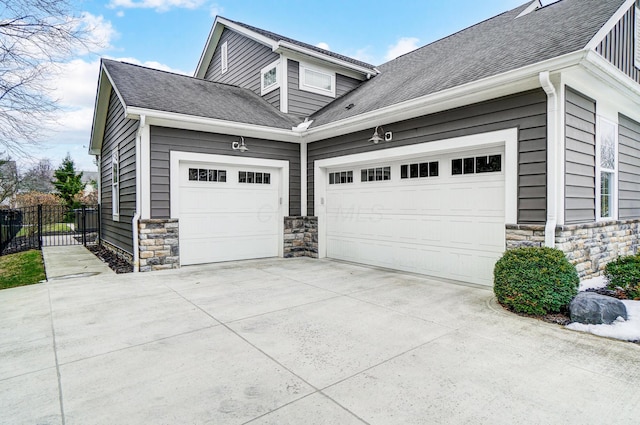 view of property exterior with stone siding, concrete driveway, an attached garage, and fence