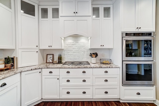 kitchen featuring appliances with stainless steel finishes, white cabinets, glass insert cabinets, and tasteful backsplash