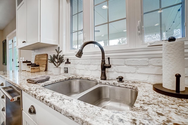 details with white cabinets, dishwasher, a sink, light stone countertops, and backsplash