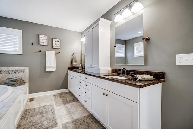 bathroom with double vanity, visible vents, a bathing tub, a sink, and baseboards