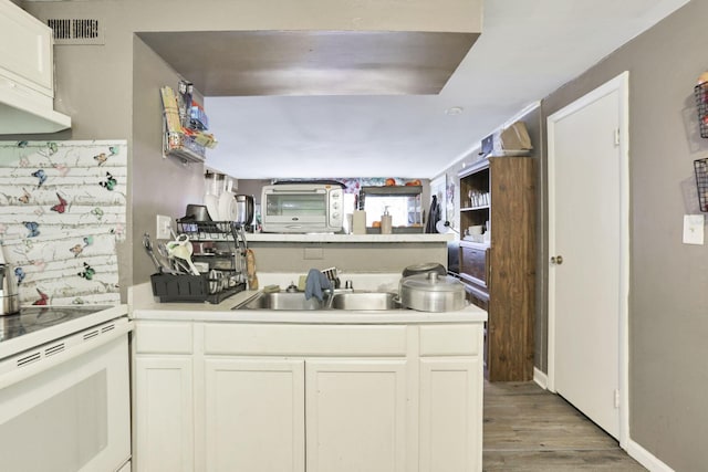 kitchen featuring light wood-type flooring, kitchen peninsula, white cabinets, and sink