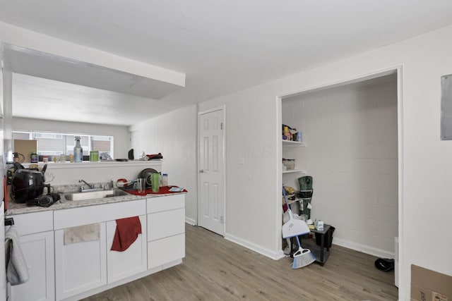 kitchen with white cabinets, sink, light stone counters, and light hardwood / wood-style floors