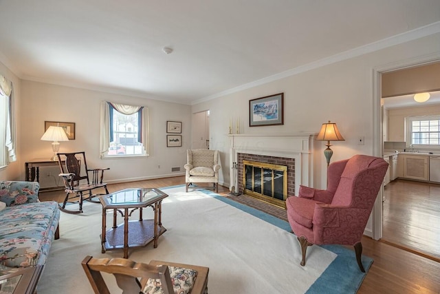 living room with sink, a brick fireplace, light hardwood / wood-style floors, and crown molding