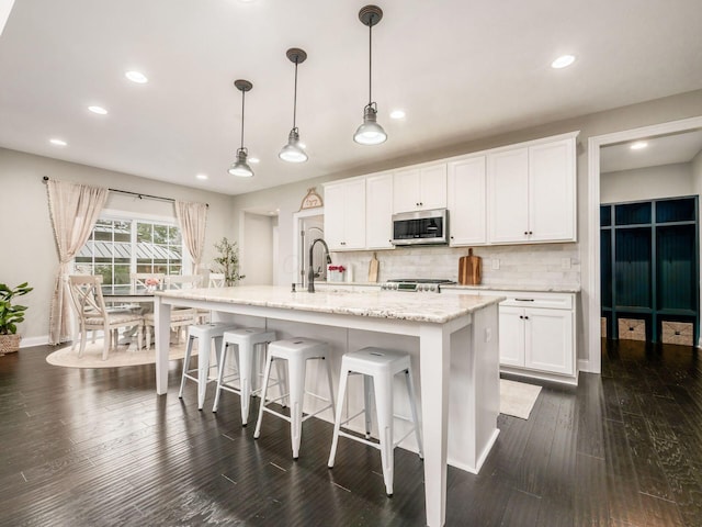 kitchen featuring backsplash, a center island with sink, hanging light fixtures, dark hardwood / wood-style floors, and white cabinetry