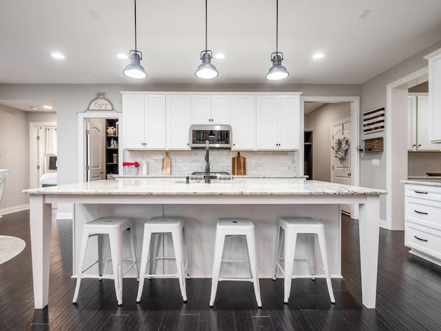 kitchen featuring a center island with sink, decorative backsplash, pendant lighting, and white cabinets