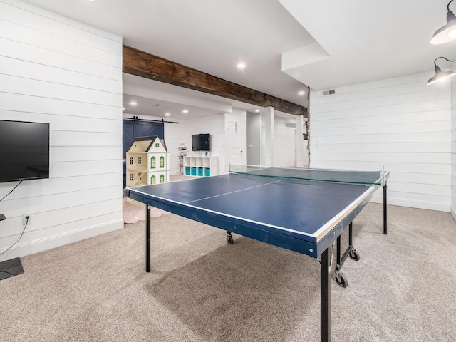 recreation room with carpet flooring, a barn door, beam ceiling, and wooden walls