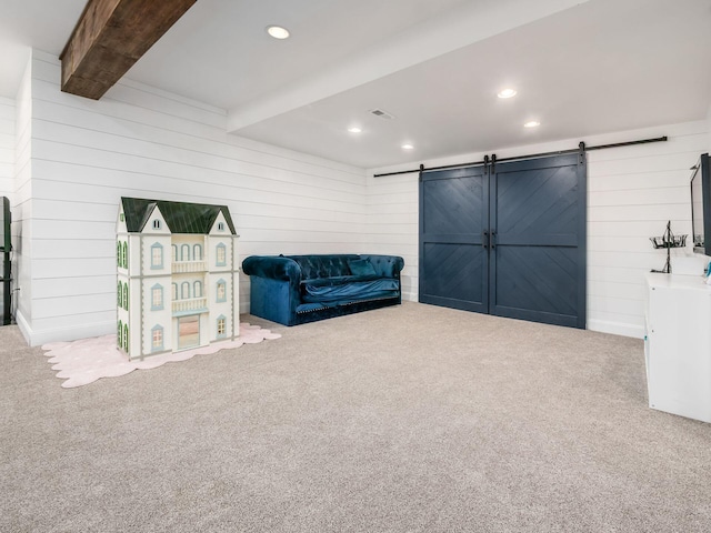 sitting room featuring beamed ceiling, carpet, a barn door, and wood walls