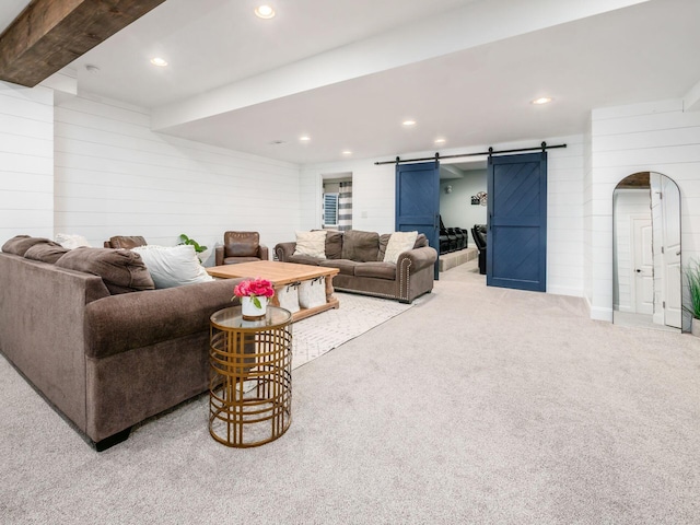 carpeted living room with wood walls, a barn door, and beam ceiling