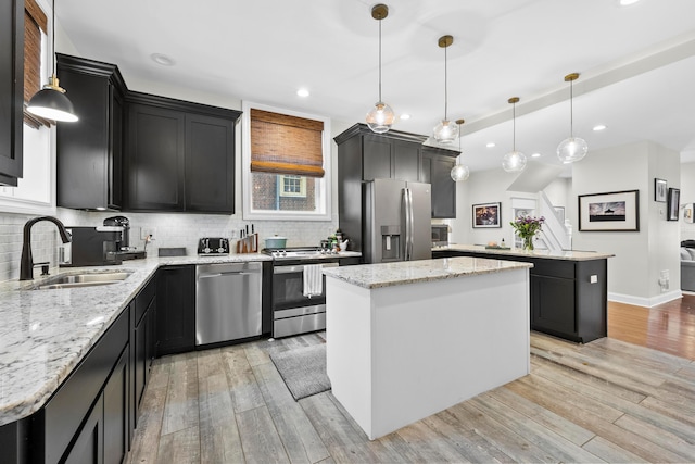 kitchen with light stone countertops, appliances with stainless steel finishes, sink, a center island, and hanging light fixtures