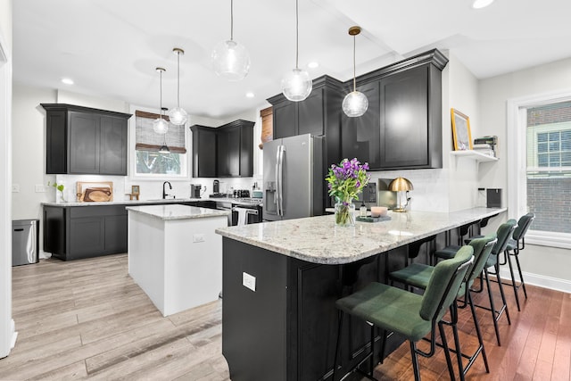 kitchen featuring pendant lighting, light wood-type flooring, stainless steel fridge with ice dispenser, and light stone counters