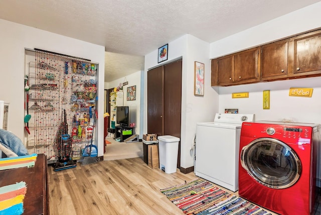 clothes washing area featuring cabinets, light wood-type flooring, a textured ceiling, and washing machine and clothes dryer