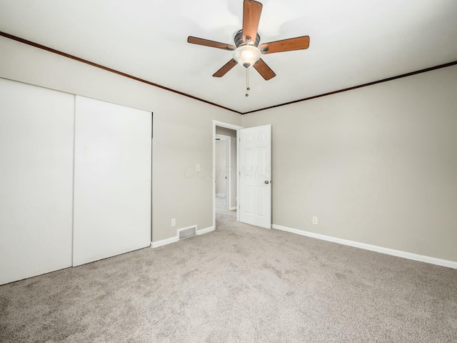 unfurnished bedroom featuring a closet, light carpet, ceiling fan, and crown molding