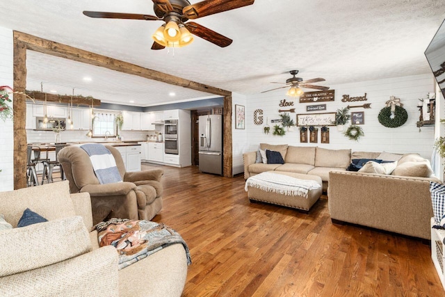 living room with beam ceiling, sink, wood-type flooring, and a textured ceiling