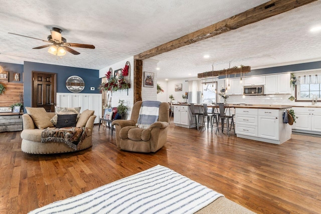 living room featuring beam ceiling, ceiling fan, sink, hardwood / wood-style floors, and a textured ceiling