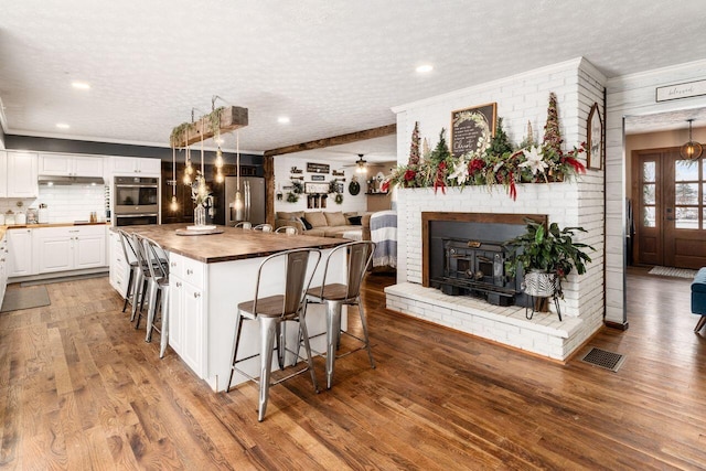 kitchen with wooden counters, a breakfast bar, a textured ceiling, stainless steel appliances, and white cabinetry