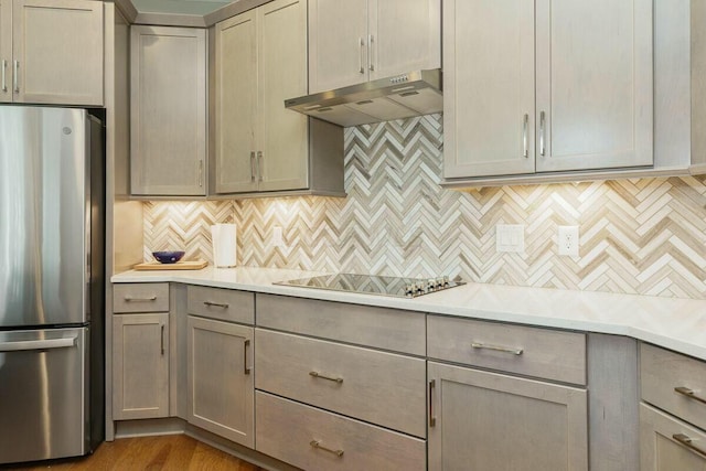 kitchen with decorative backsplash, light wood-type flooring, black cooktop, gray cabinets, and stainless steel refrigerator