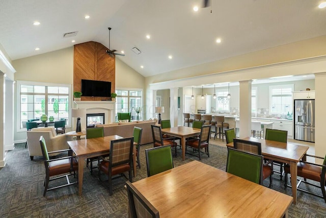 dining room with a fireplace, dark colored carpet, high vaulted ceiling, and ceiling fan