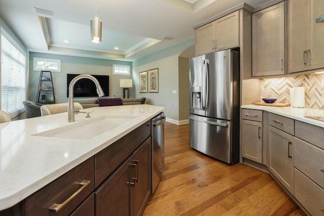 kitchen with sink, a raised ceiling, tasteful backsplash, pendant lighting, and appliances with stainless steel finishes