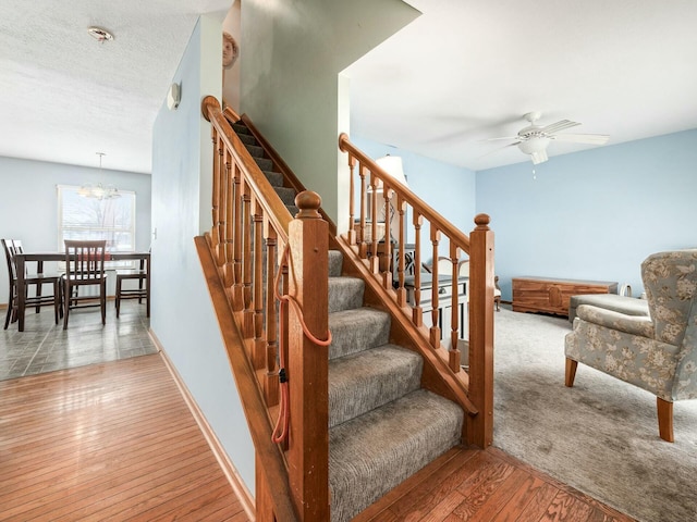 stairs featuring hardwood / wood-style floors, ceiling fan with notable chandelier, and a textured ceiling