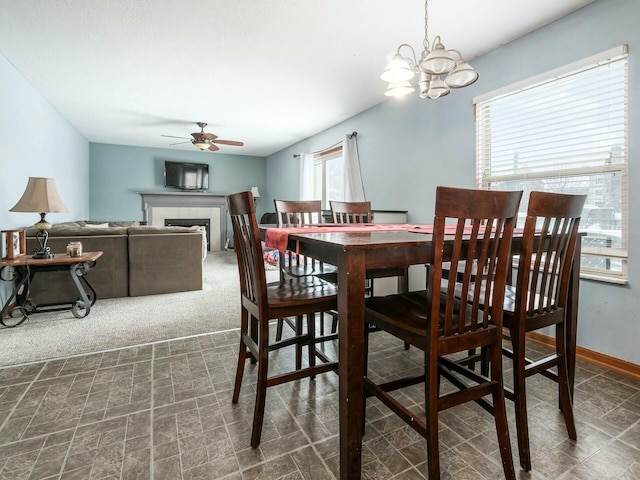 carpeted dining room with a tiled fireplace and ceiling fan with notable chandelier