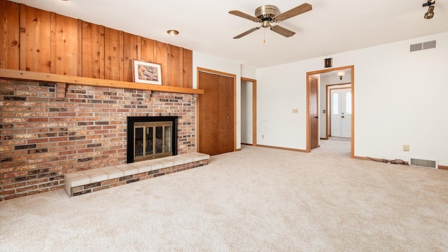 unfurnished living room with ceiling fan, carpet floors, wood walls, and a brick fireplace