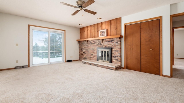 unfurnished living room featuring a fireplace, carpet flooring, ceiling fan, and wooden walls