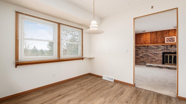 spare room with wooden walls, a fireplace, and light hardwood / wood-style floors