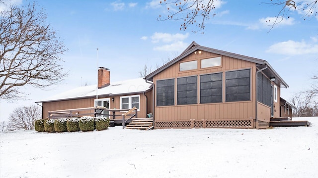 snow covered back of property featuring a sunroom and a deck