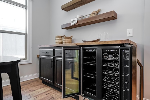 bar with a wealth of natural light, beverage cooler, and light hardwood / wood-style floors