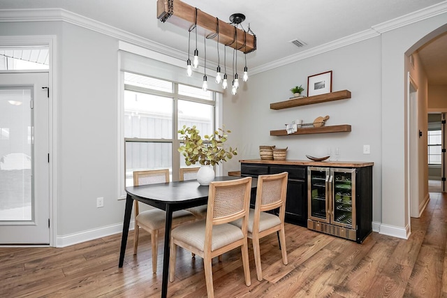 dining room featuring bar area, ornamental molding, beverage cooler, and light hardwood / wood-style flooring