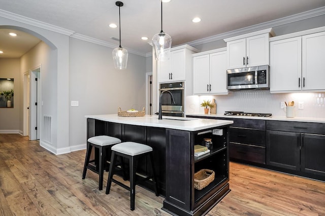 kitchen with white cabinets, light wood-type flooring, an island with sink, tasteful backsplash, and stainless steel appliances