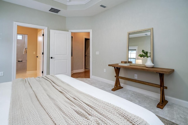 bedroom with light carpet, connected bathroom, a tray ceiling, and ornamental molding