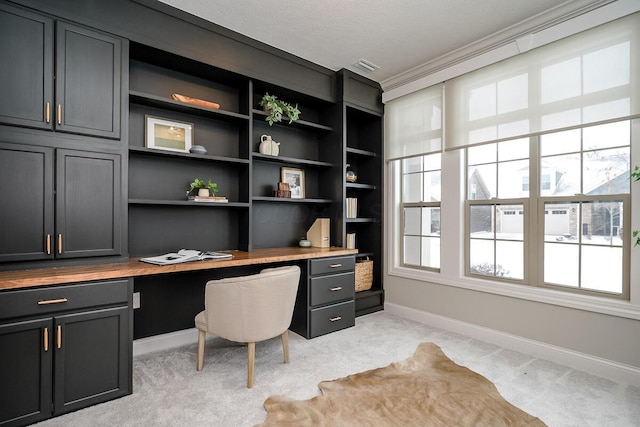 carpeted office space featuring built in shelves, crown molding, and built in desk