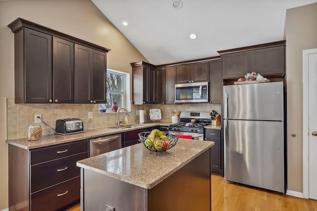 kitchen featuring light stone counters, stainless steel appliances, sink, a center island, and lofted ceiling