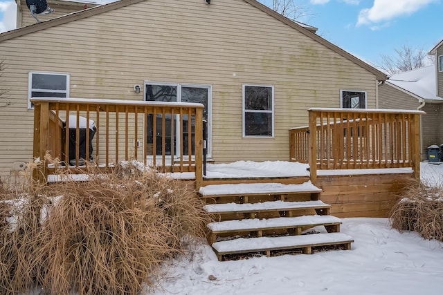 snow covered back of property with a wooden deck