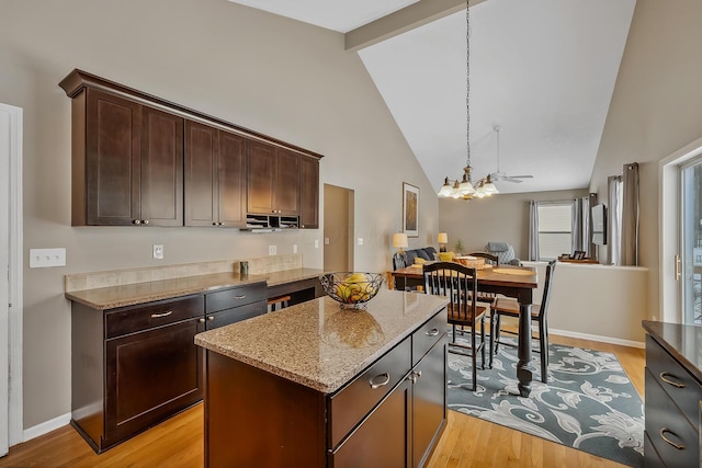 kitchen featuring beam ceiling, dark brown cabinetry, light stone countertops, light hardwood / wood-style floors, and a kitchen island