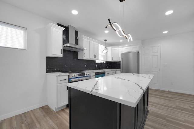 kitchen with wall chimney exhaust hood, stainless steel appliances, white cabinetry, a kitchen island, and hanging light fixtures