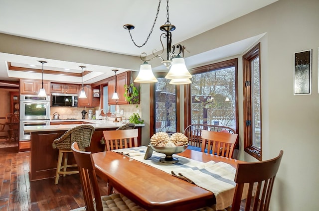 dining room with dark hardwood / wood-style flooring, an inviting chandelier, a raised ceiling, and sink