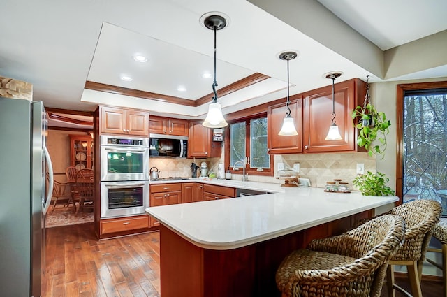 kitchen with kitchen peninsula, a breakfast bar, stainless steel appliances, a raised ceiling, and pendant lighting